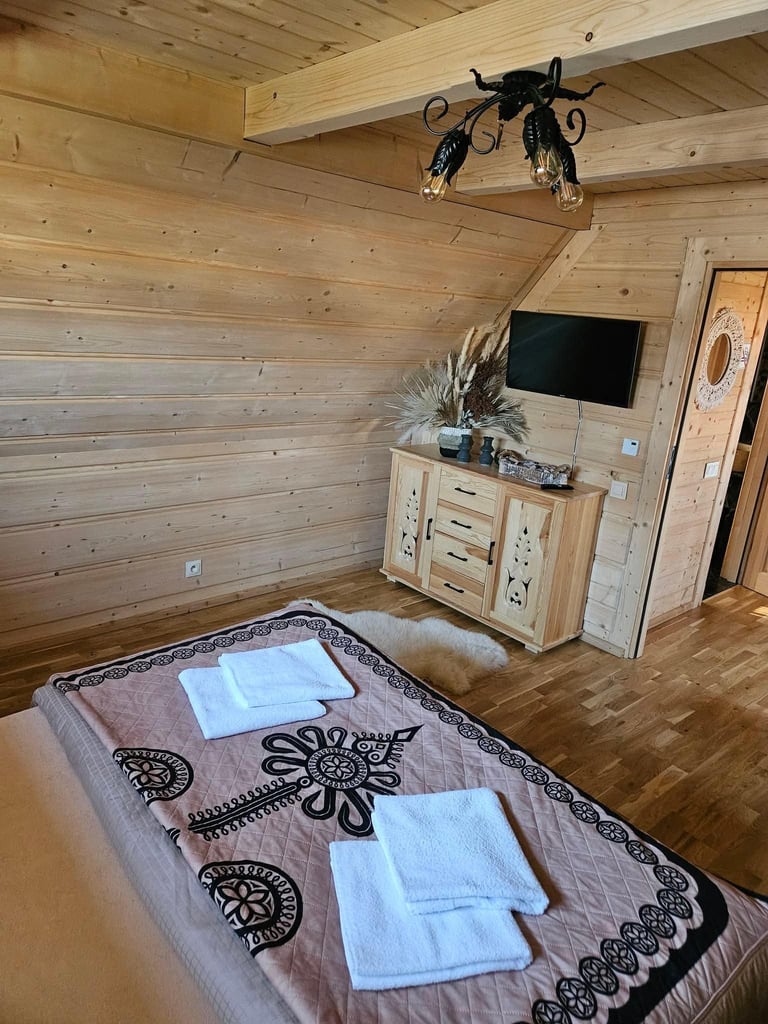 Sypialnia w chatce z łóżkiem, telewizorem na komodzie i czarnym kutym żyrandolem